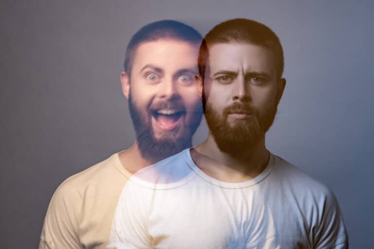 Ein bärtiger Mann erscheint zweimal im Bild: Die eine Version sieht ernst aus, während die sich überlagernde, durchscheinende Version auf der linken Seite große Augen hat und enthusiastisch lächelt. Beide tragen weiße T-Shirts vor einem neutralen Hintergrund.